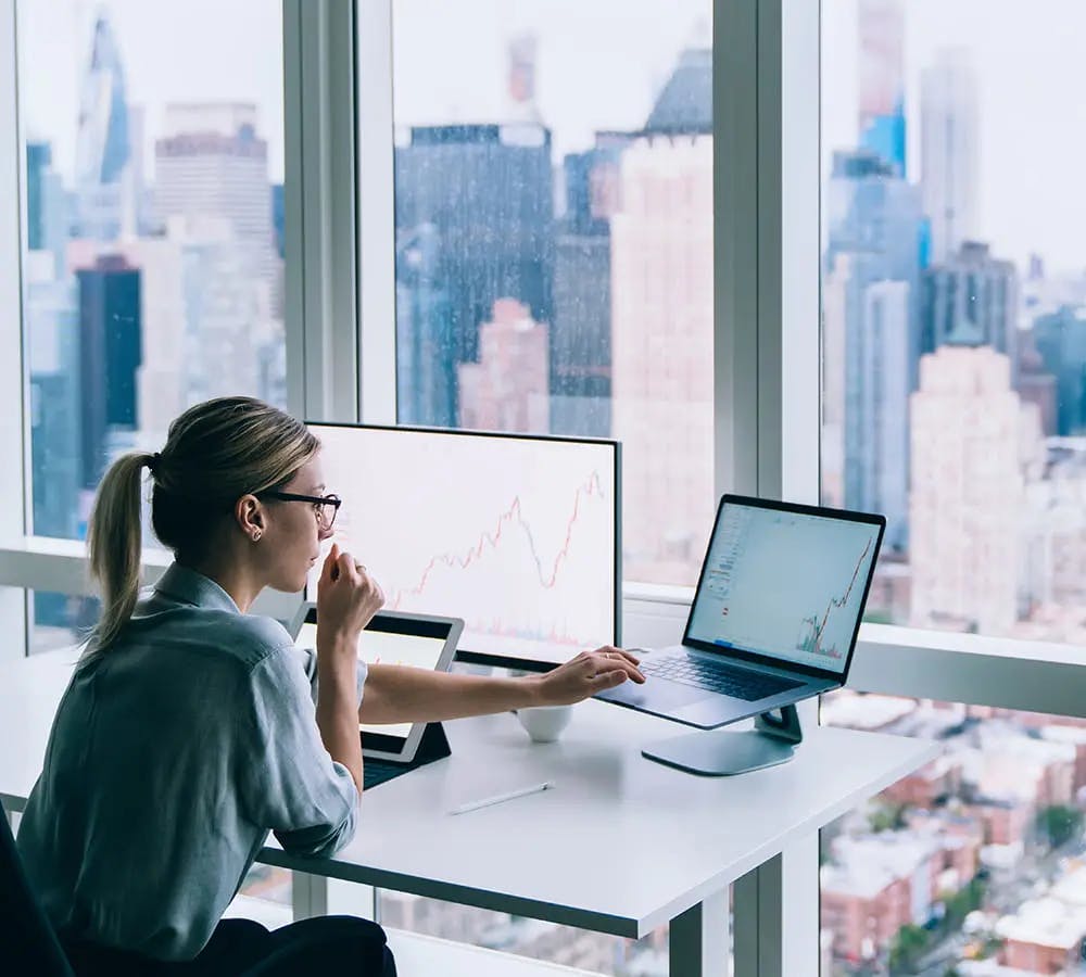 A woman sitting at her desk in front of a window overlooking a sprawling city.